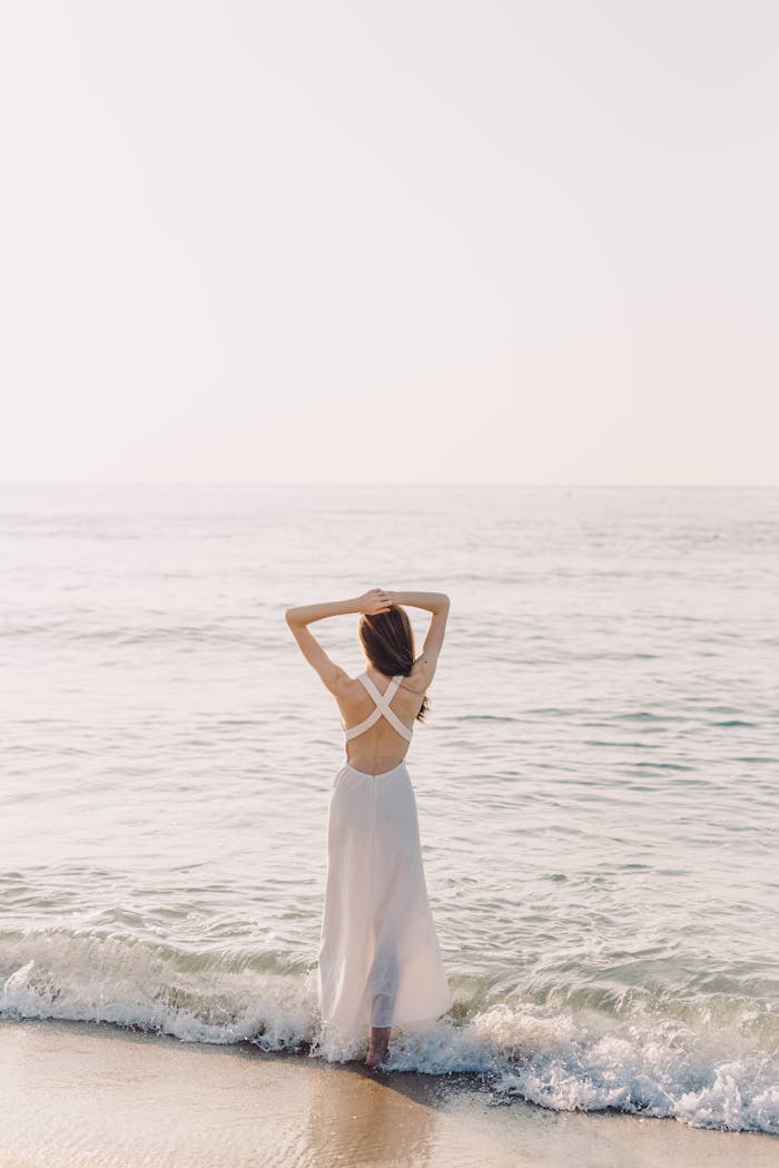 Woman stands on a serene beach at sunrise, embracing summer vibes and tranquility.
